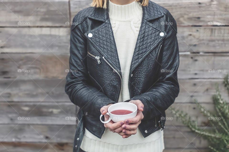 Leather Jacket And Tea
Woman wearing black leather jacket holding a cup of tea standing in front of wooden wall.