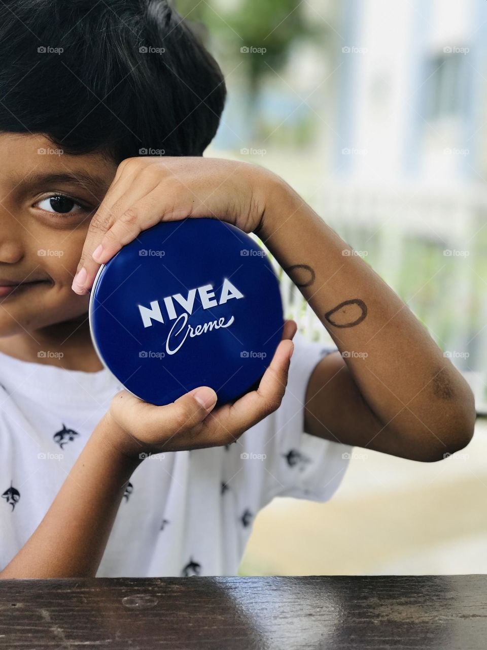 A cheerful boy holds Nivea cream in his both hands.