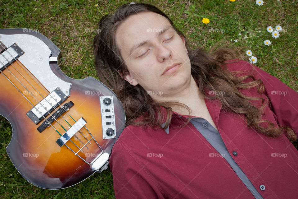 Youth lying with a bass guitar on grass
