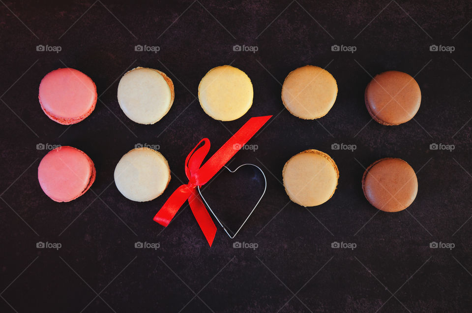 Background of the colorful delicious macaroons at dark table close up. Valentine's day. Greetings card. Flat lay.