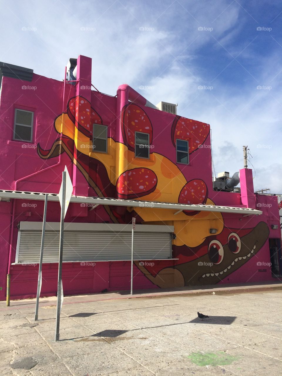 Wall in Venice Beach, California painted hot pink with a piece of smiling cheesy pepperoni pizza
