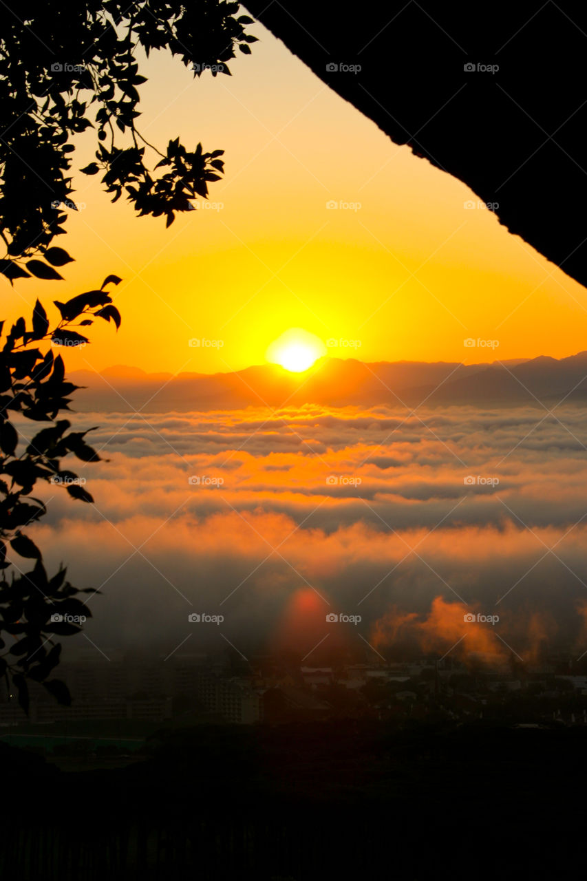 Sunrise over valley with clouds with tree framing sunset