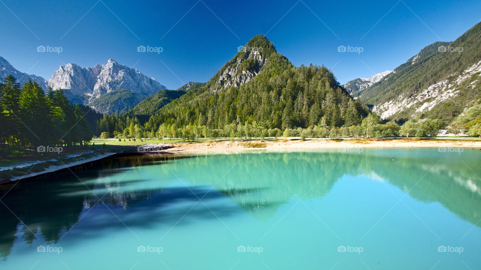 Alpine lake with a pyramid-shaped mountain covered with green fir trees.