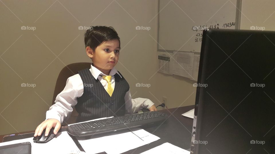 kid wearing business attirel, sitting at a desk in front of a computer