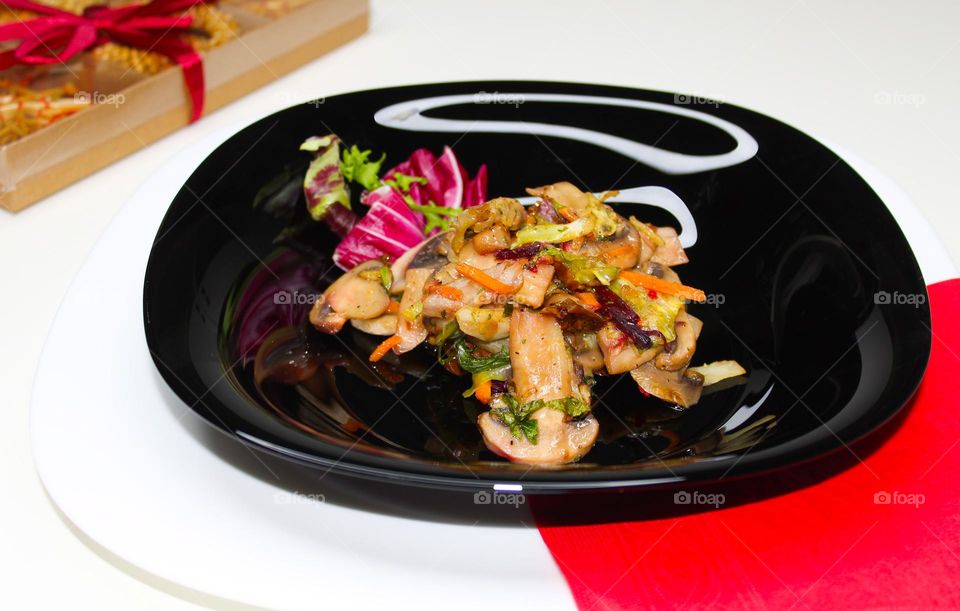 Stewed mushrooms with vegetables on a black plate.  Angle view of food