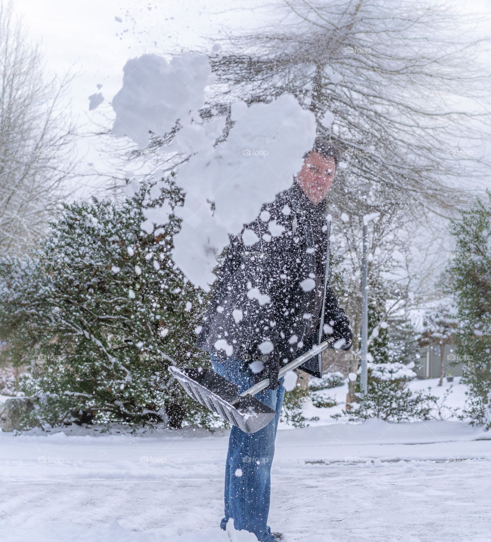 Man shoveling snow and throwing it to the side of his driveway after a winter snowfall 