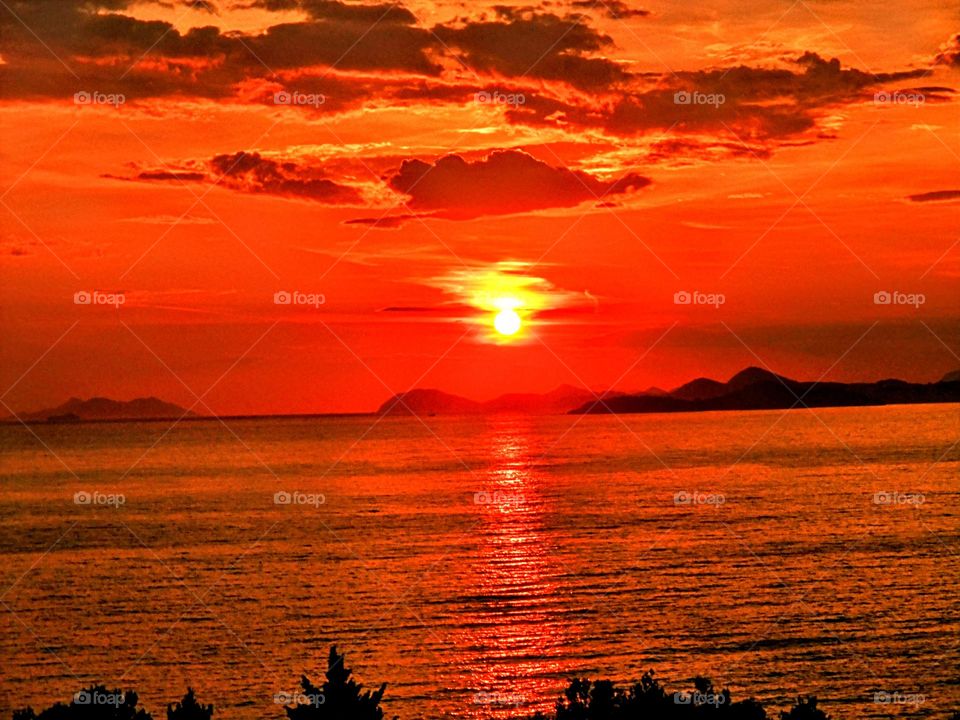 Vivid red sunset with a glowing yellow sun reflected across the sea with mountains silhouetted in the background