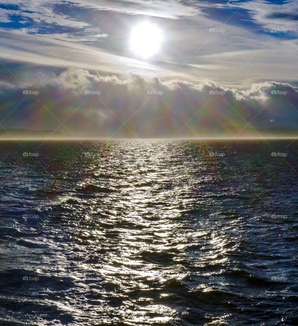 Sun reflects through cloudy sky on ocean ripples 