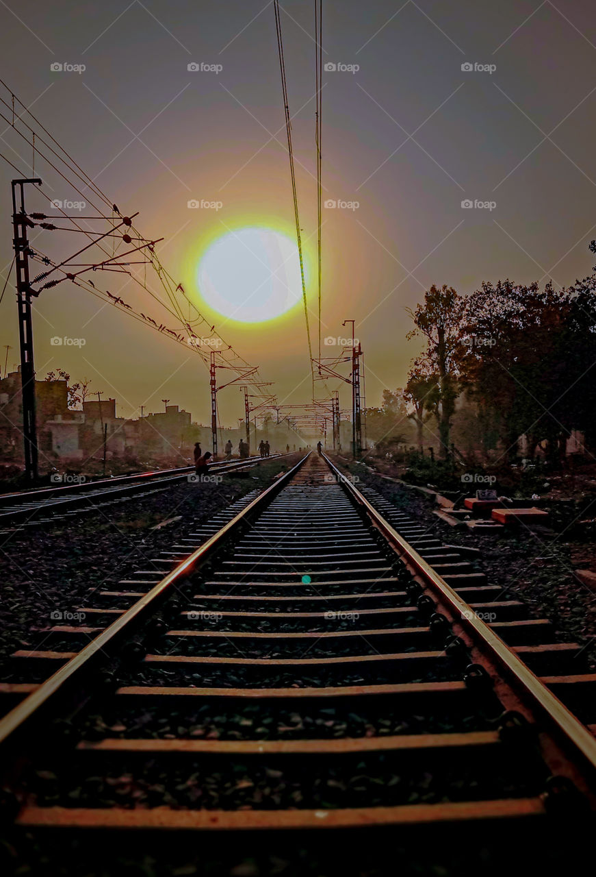 how can I describe this morning photo
this railway tracks, the huge shining sun of summer,  people who crossing this railway tracks, wire poles in row,  the green🌳 trees around tracks, the patterns created by logs, and beautiful colour of summer nat