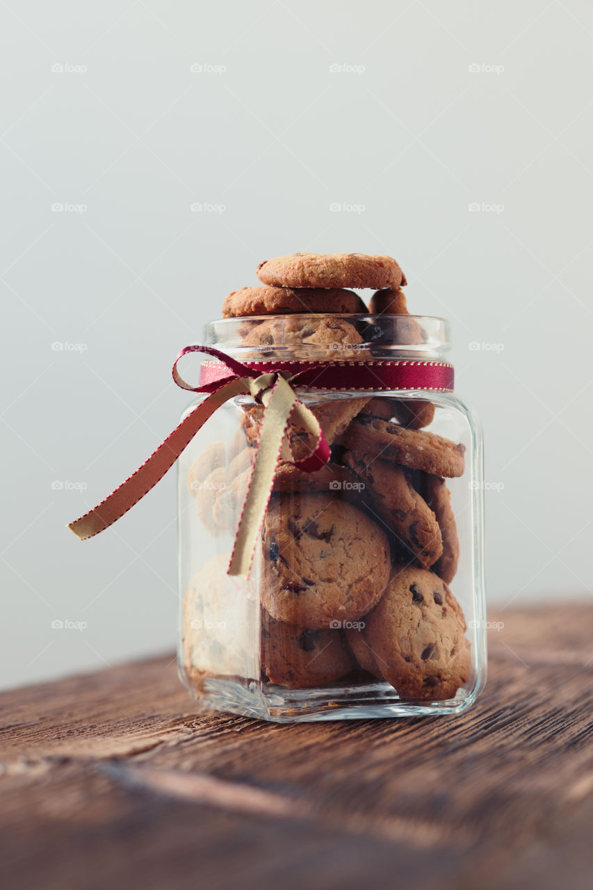 Big jar filled with oat cookies standing on a wooden table. Plain background. Portrait orientation