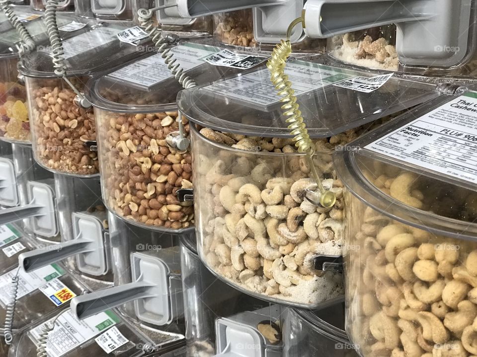 Bins of various delicious nuts with scoops in the bulk foods section of a grocery store. 