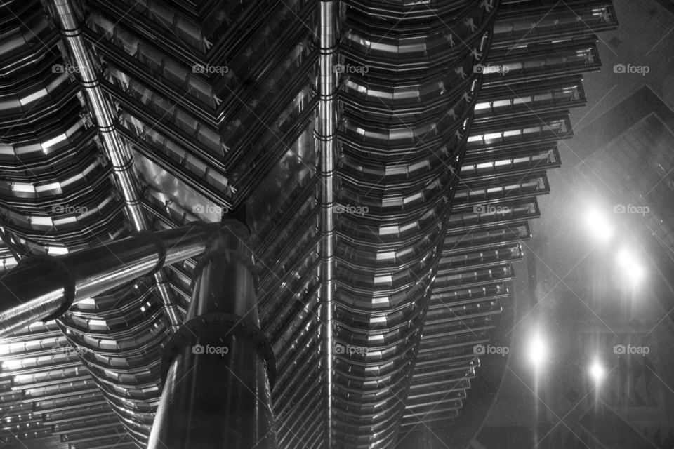 View from Petronas tower. View downward from Petronas tower during rain storm. Bright spotlights on the ground. Support beam for viewing deck