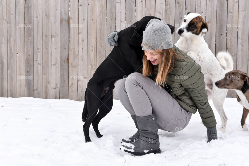 Young woman laughing and playing with her dogs outdoors in the snow during winter