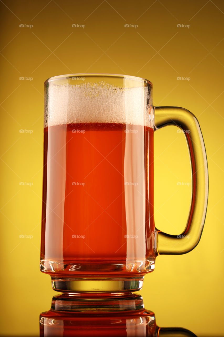 Glass full of beer with froth on yellow background