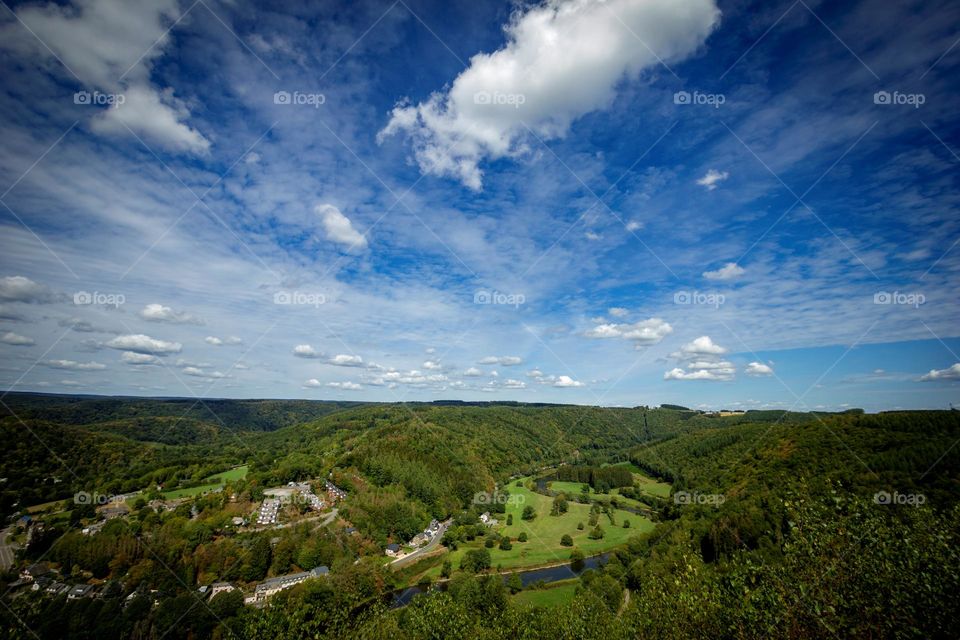 A portrait of the landscape of the belgium ardennes in the vresse sur semois region with a blue sky with some clouds in it.