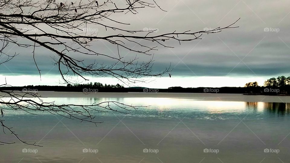 overcast dawn.  sunlight peeking out beyond the cloud cover reflecting light on the lake.