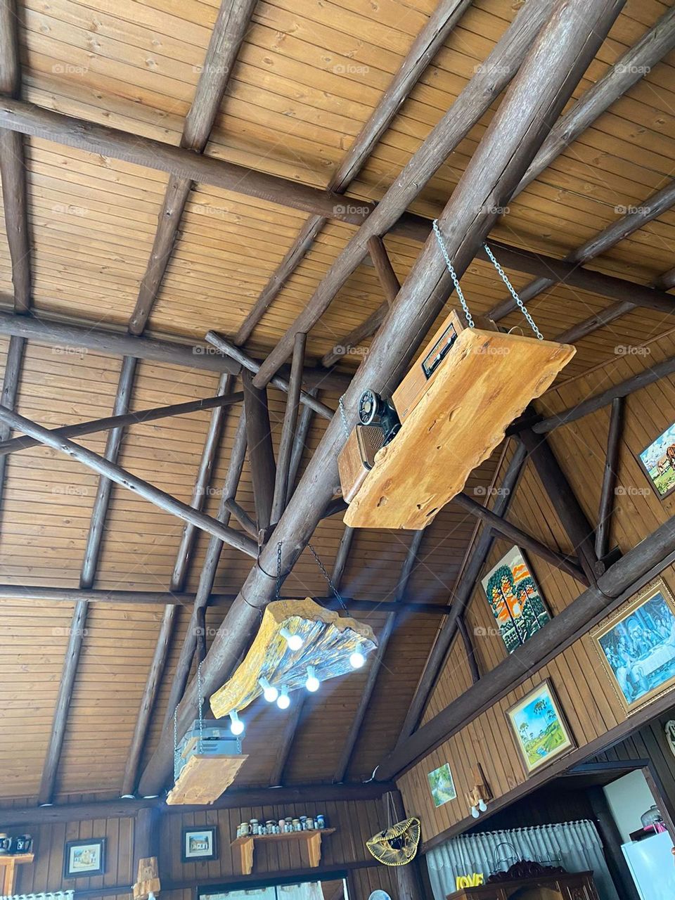 Casa de campo, residência antiga com lâmpadas incrustadas na madeira. Quadros diversificados pendurados na parede, bem no alto.