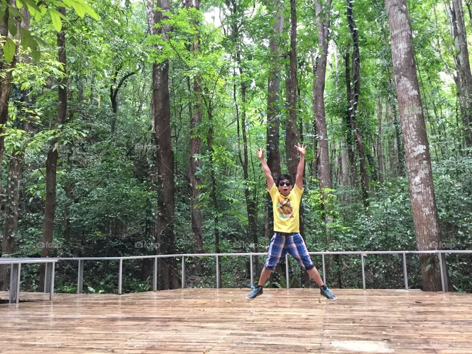 A boy jumping with a beautiful green forest as a background.