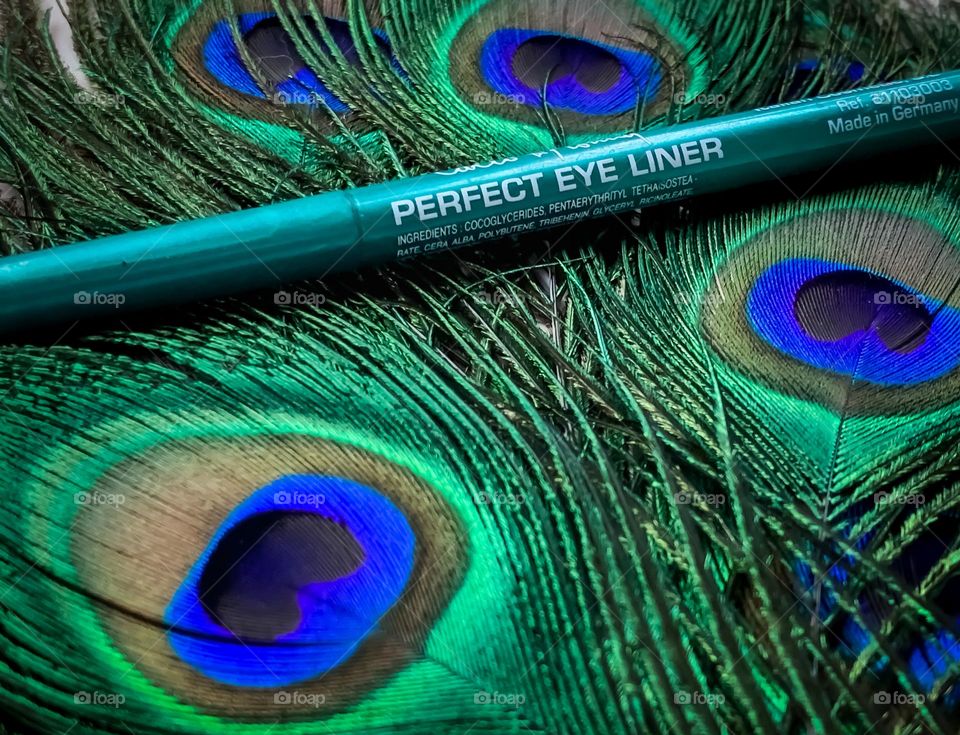 Green eyeliner displayed on a bed on peacock feathers