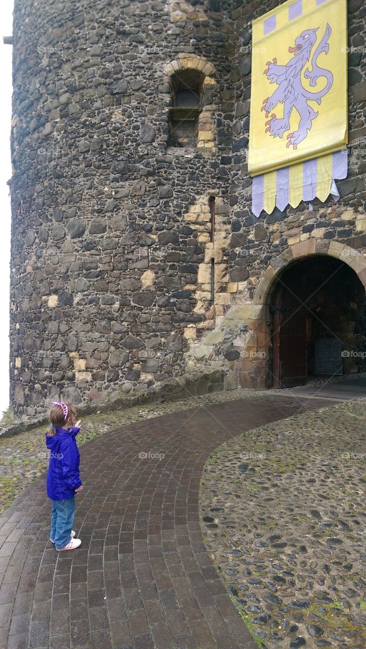 small girl standing in front of entrance to anciant stone castle