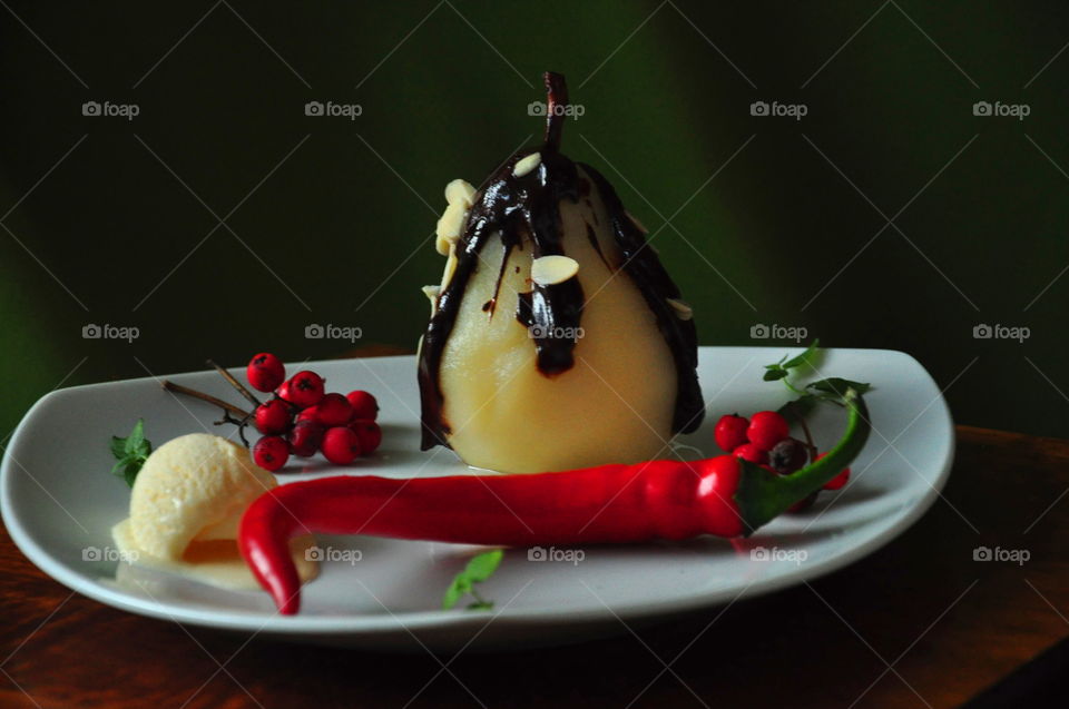 autumn dessert pear in chocolate and almond with ice cream berry and chili on white plate