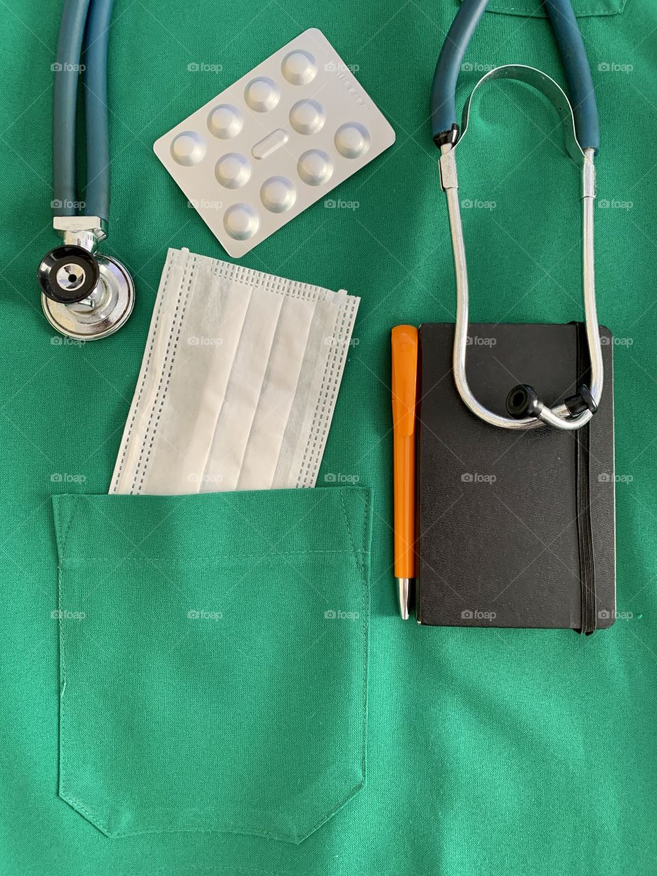 Health professional material: Medical scrub with pills, notebook, pen, surgical mask and stethoscope.