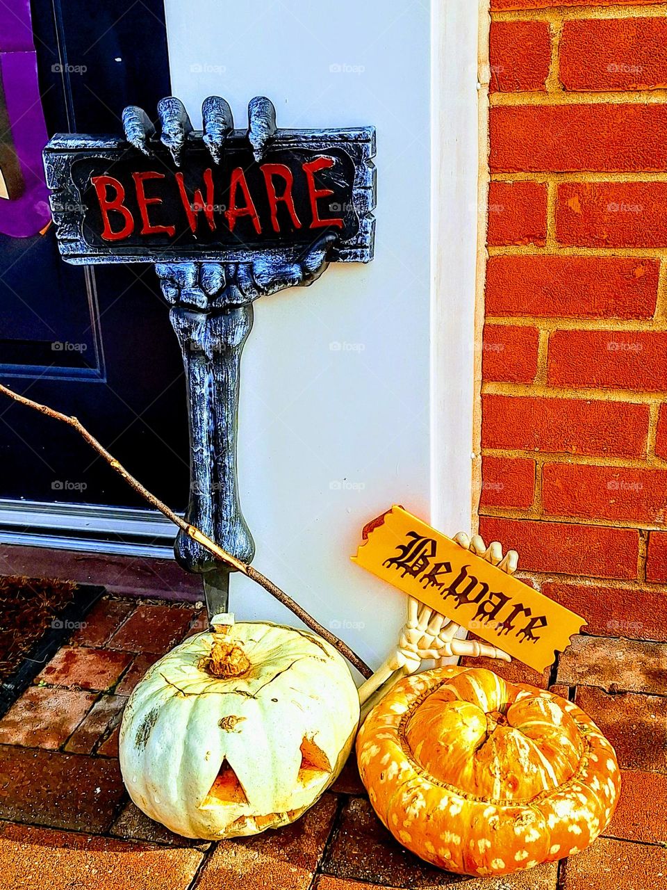 Halloween display with two unusual pumpkin varieties, a skeletal hand holding a Beware sign against a bright red brick wall