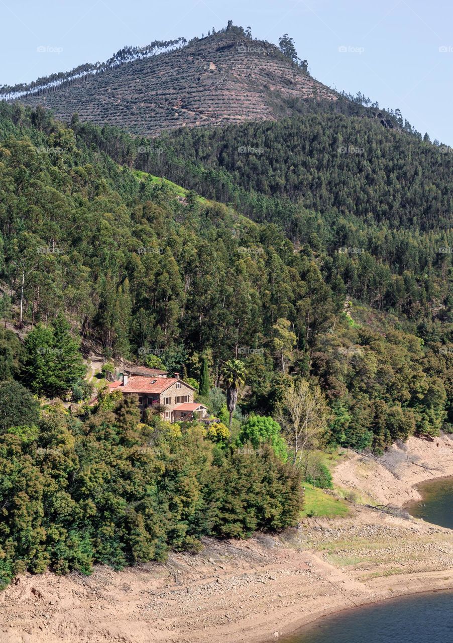 A stone lodge sits beneath a tree covered mountain and on the banks of the Rio Zêzere, near Dornes in Central Portugal 