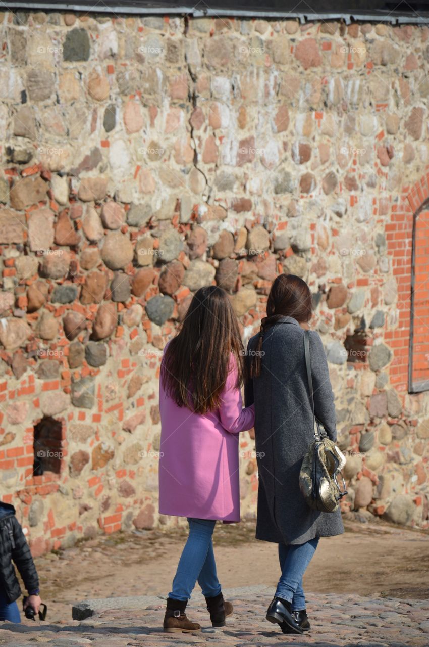 Rear view of two woman walking near stone wall