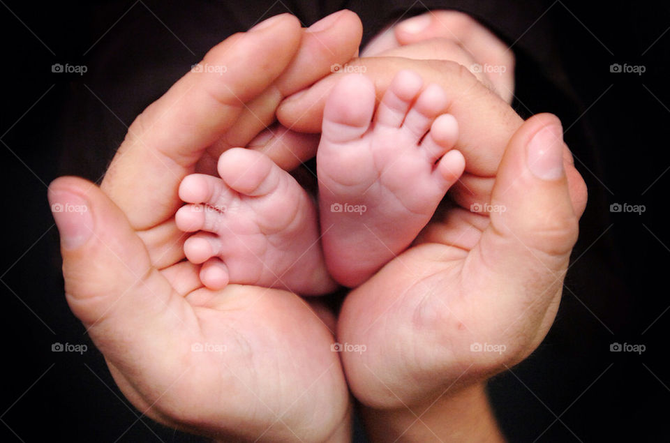 The feet if a newborn white baby are cupped in the hands of a white