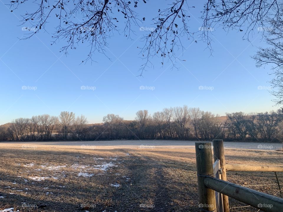 View from a wooden gate across an empty farm field to bare trees in distant hills on a beautiful autumn day- landscape