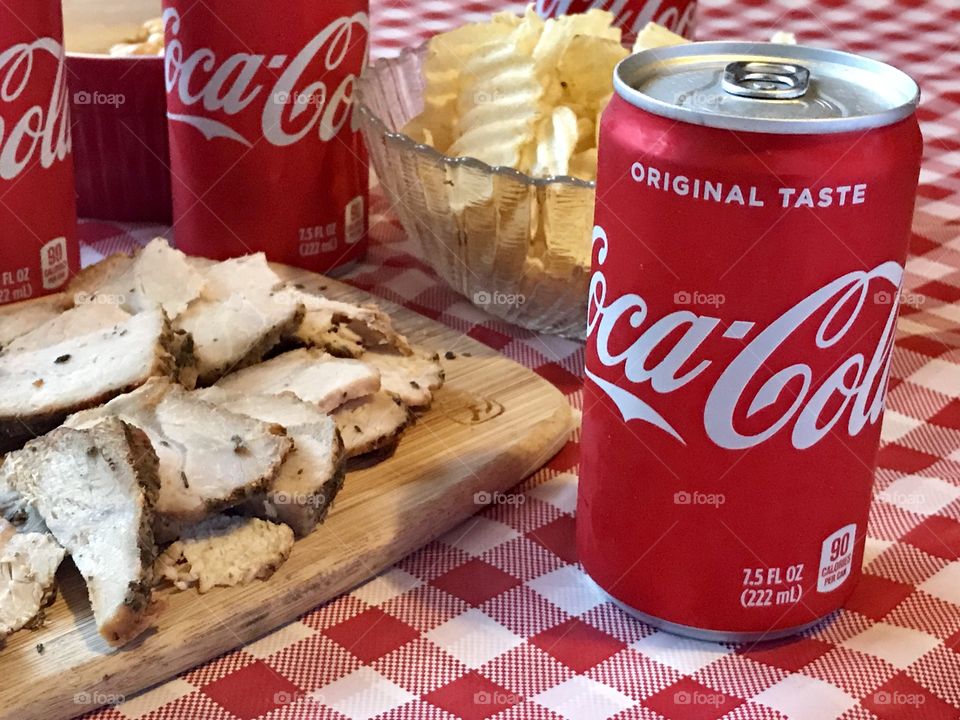 Cans of Coca-Cola on a red and white checkered background with barbecue food and potato chips 