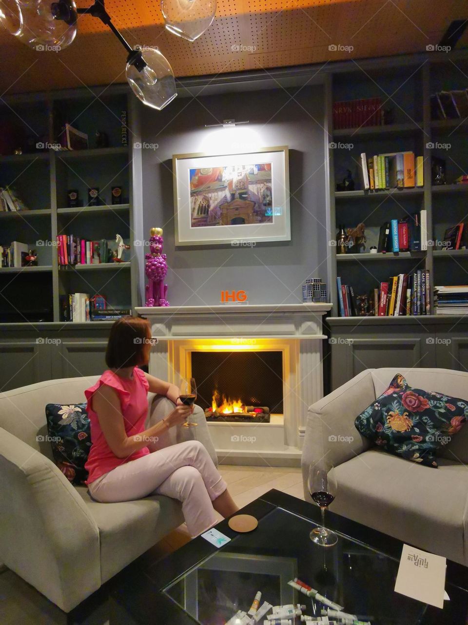 Cozy and lovely place. A woman with a glass of wine looks at the fireplace. Room for reading and relaxation.