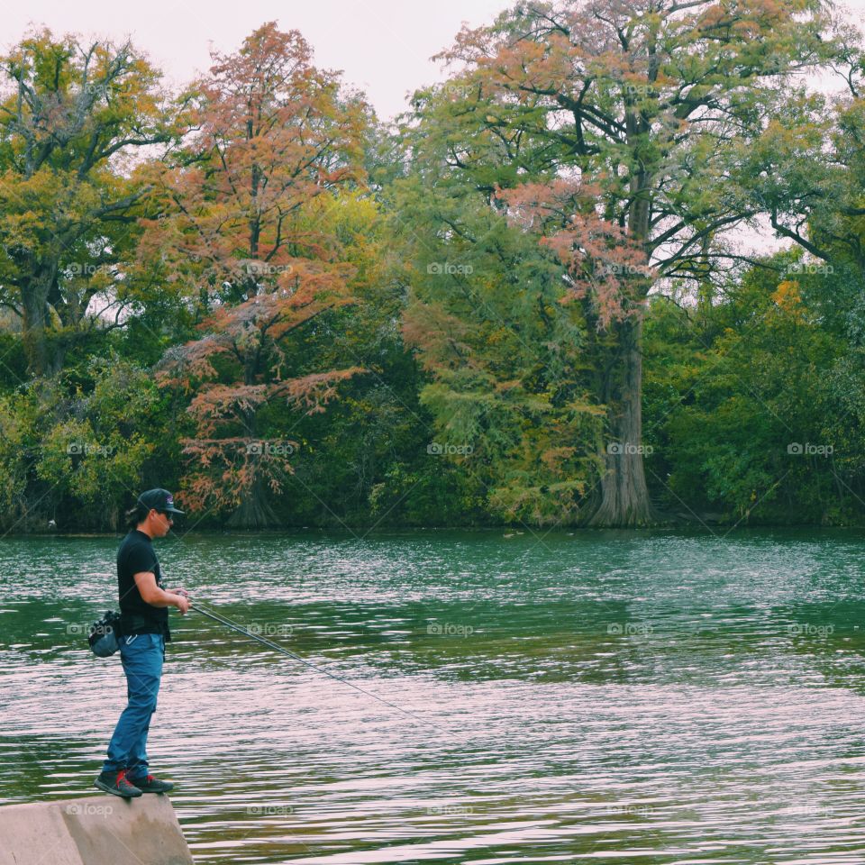 Fisherman standing on rock at lake in autumn