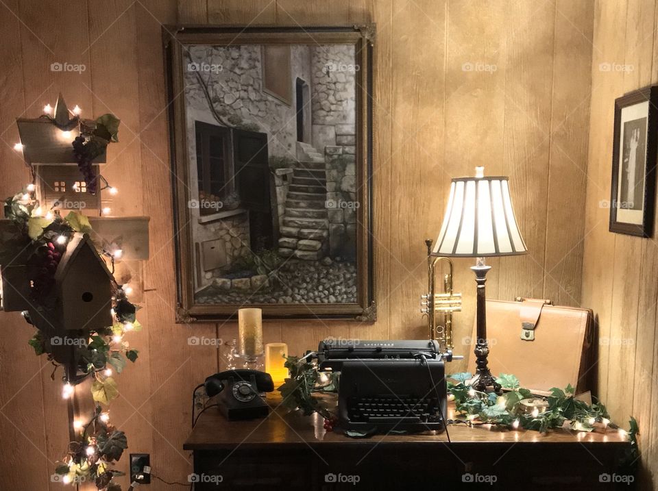 Still life, lamp with a beige satchel and an old typewriter and old phone on a desk.  Paintings on the wall. Old fashioned elegant look.