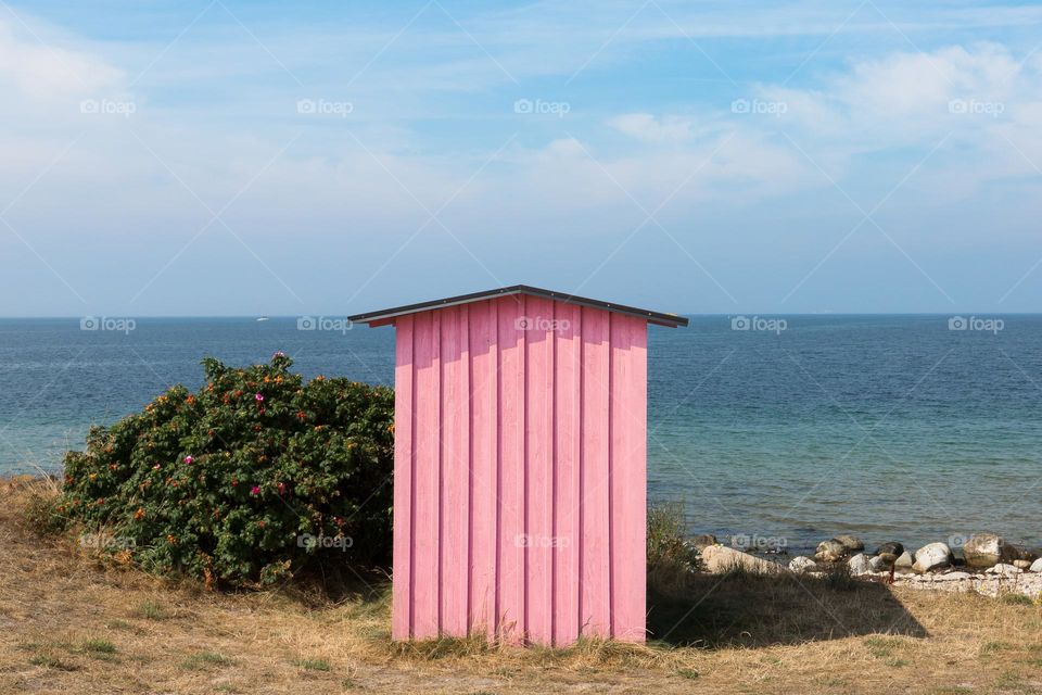 A small bright pink hut by the blue ocean on a sunny summer day 
