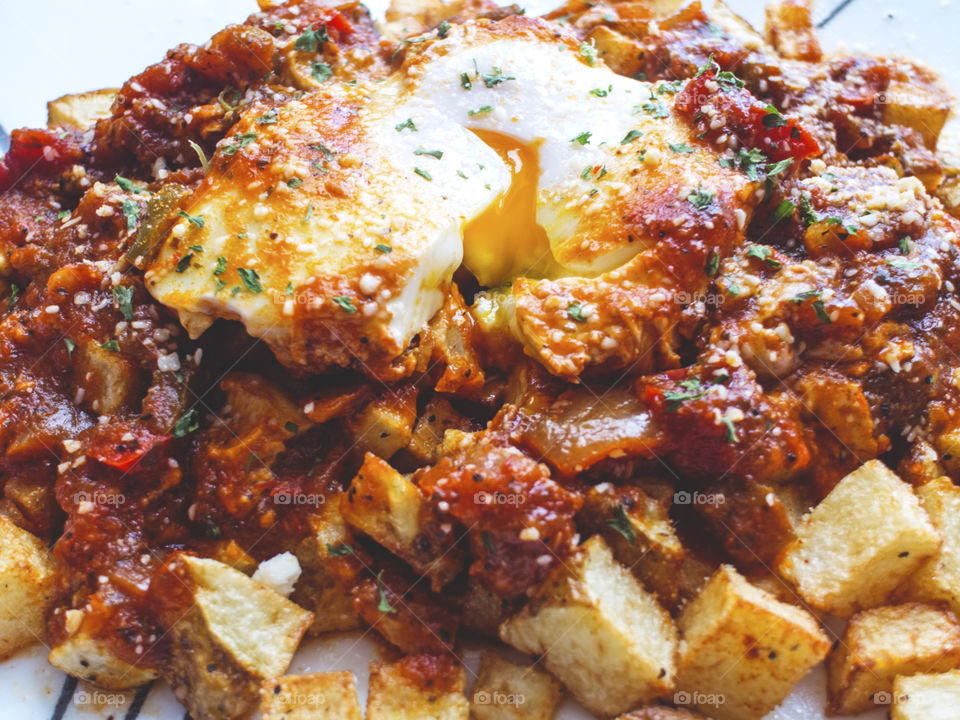 Closeup of poached egg on fried potatoes with tomato sauce