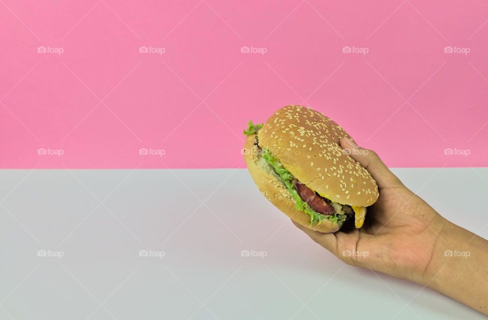 Delivery of hamburger in hand with pink and white background. Fast street food