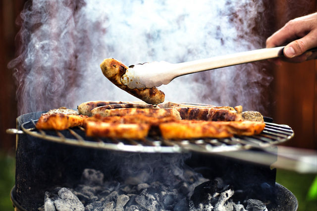 Person grilling sausage on barbecue