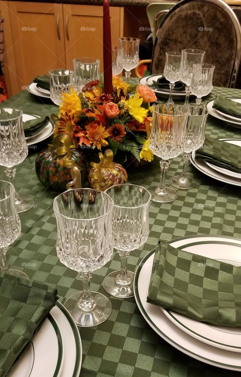 Harvest bouquet in a decorative vase gracefully adorning the thanksgiving table, with the good crystal and plates, with glass pumpkins 