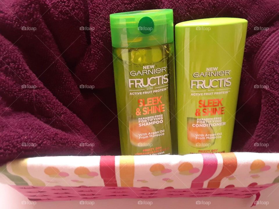 Garnier Fructis Shampoo and Conditioner in a basket. The Garnier Fructis products are laying upright against a towel, which is also in the basket.