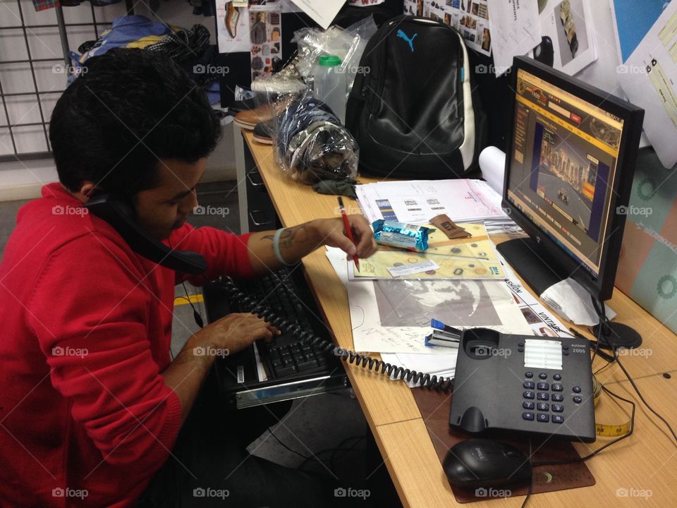 Multi tasking. A guy answering phone, writing notes and working in computer