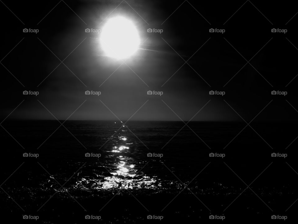 The silver light from the glowing orb in the sky turns the ocean into glistening waves.