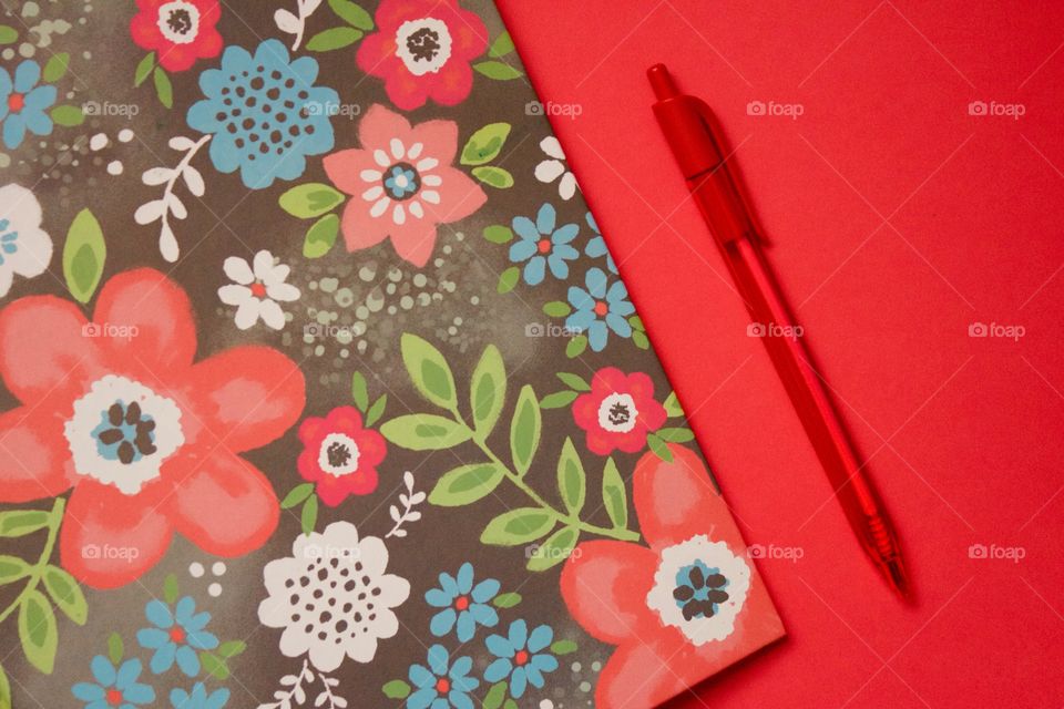 Flat lay of a multi-colored floral binder and red pen on a red background 