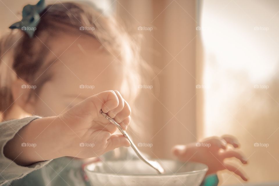 Your girl learning to eat cereal. . Early morning child eating cereal, holding a spoon