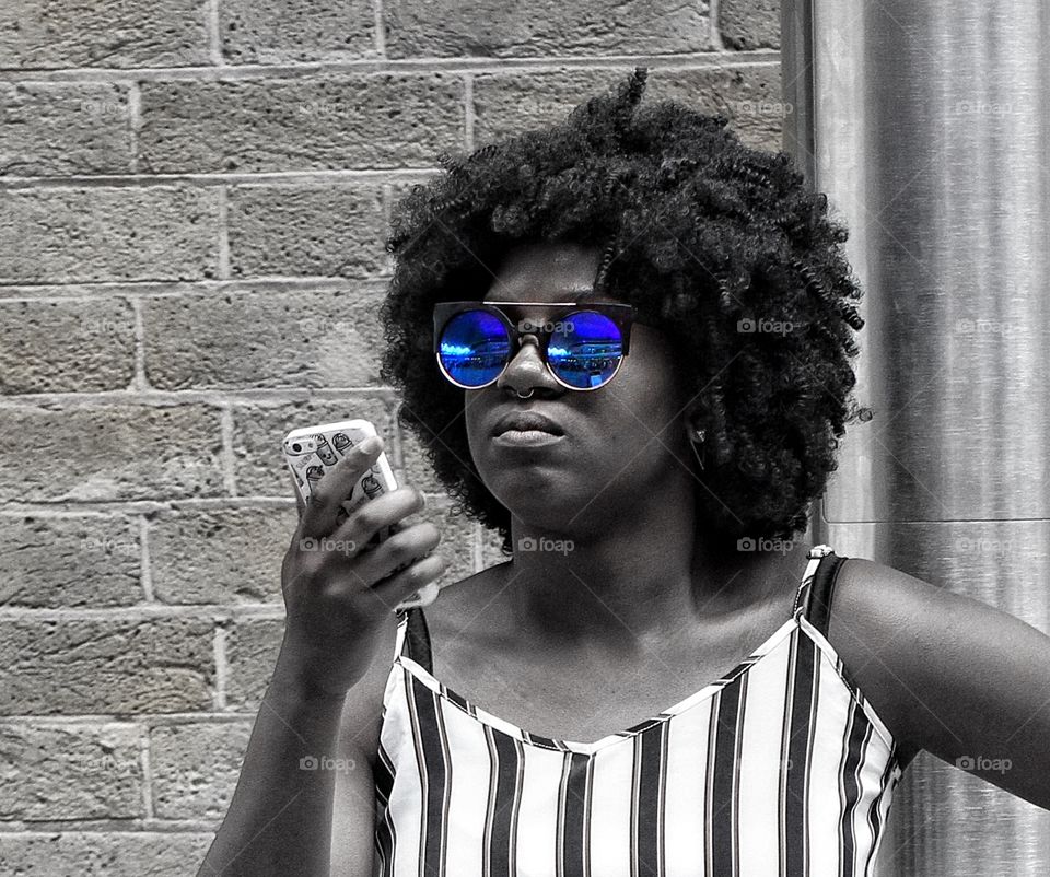 A fashionable, young black woman with a large Afro checking her mobile phone for messages. A colour pop picture.