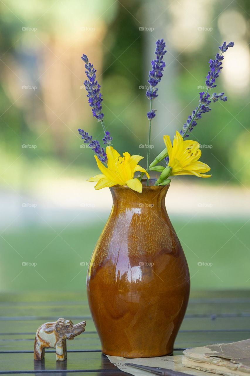 Lavender flowers and day lilies in a vase on a table outside in backyard 