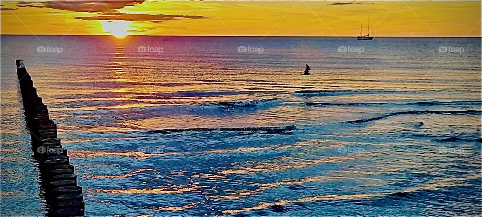 This is an intense orange  golden glowing sunset over the German „Ostsee“, the „Eastern Sea“ near „Rostock“ an important harbor town. The waves are reflecting the colors of the setting sun that are mixing with its own. 2022. Hypnotic Productions