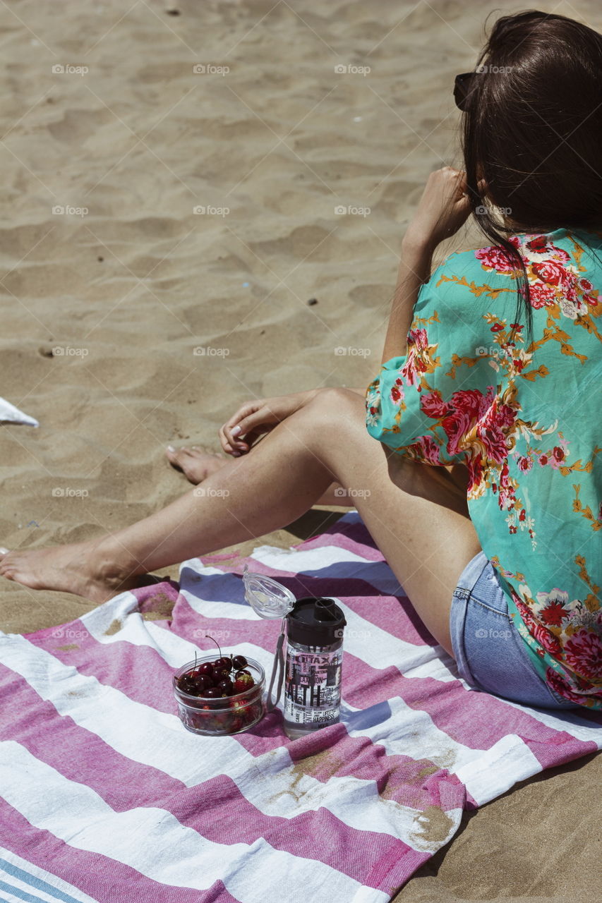 girl sitting on the sand eating fruits and drinking water