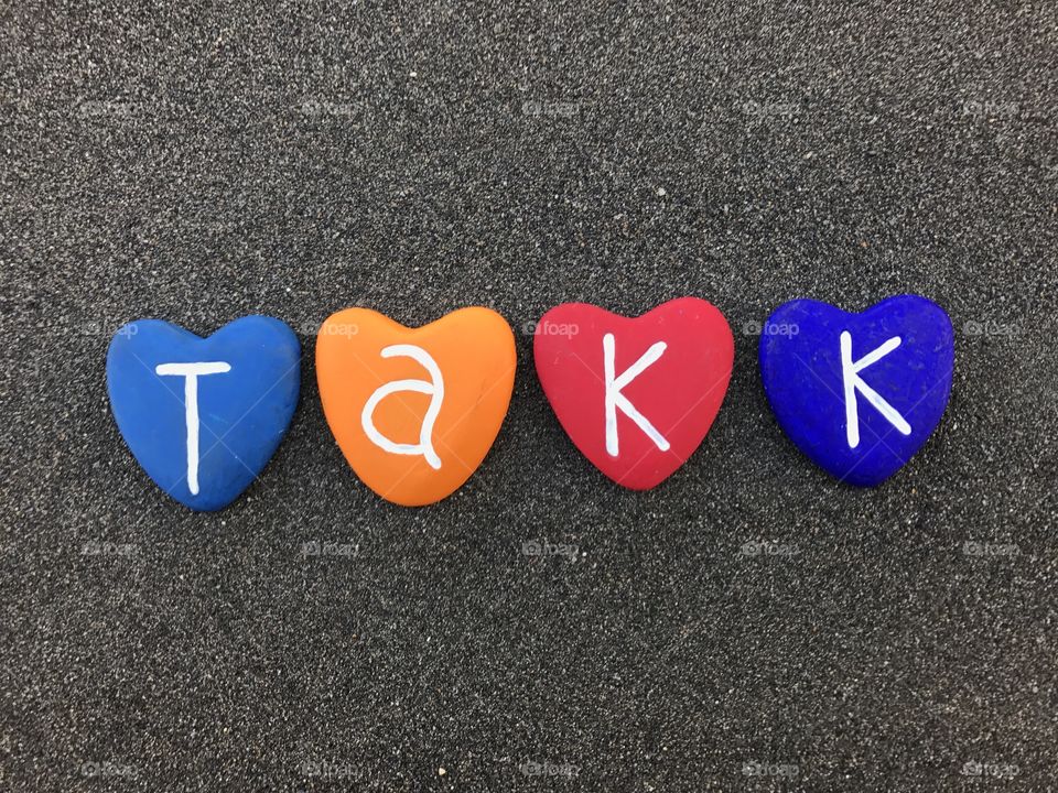 Takk, norwegian thank you with colored heart stones over black volcanic sand